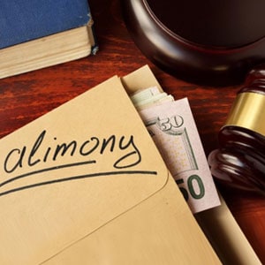 Close-up of legal desk setup: 'Alimony' envelope with $50 cash, a gavel, worn blue book, and mysterious round wooden object on dark surface.
