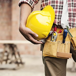 A man holding a hard hat and plaid shirt holding a tool belt - The Emory Law Firm