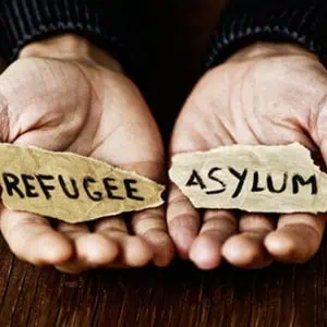 Young man's hands holding 'refugee' and 'asylum' papers dramatically. - The Emory Law FIRM PC.