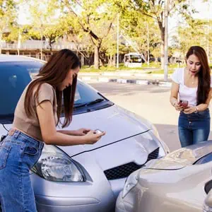 Womens photographing damage after a car accident, highlighting steps to take after a collision - The Emory Law FIRM PC